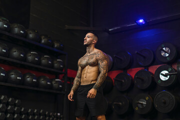 Fototapeta na wymiar Chico joven tatuado y musculoso posando con iluminación de estudio en gimnasio de crossfit