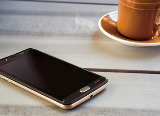 A smartphone on a table with a cup of coffee in the upper right corner