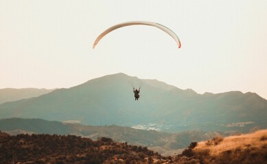 Person paragliding over a mountain range with mountains in the background
