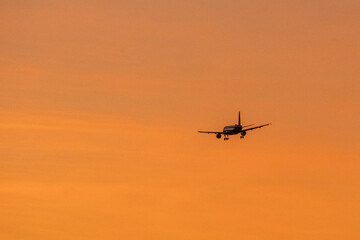 Fototapeta na wymiar Avion en vol dans un ciel orange au coucher de soleil 