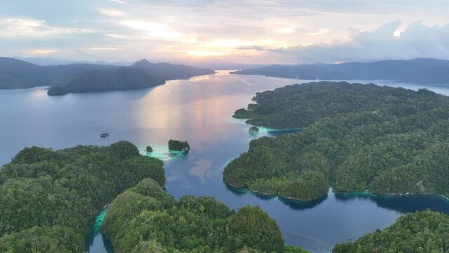 A serene sunrise illuminates the calm seas of Raja Ampat, Indonesia. This remote, equatorial region is known for its high marine biodiversity and is a popular destination for diving and snorkeling.