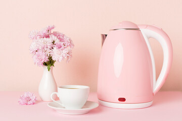 Pink electric kettle with cup of coffee and dessert on table