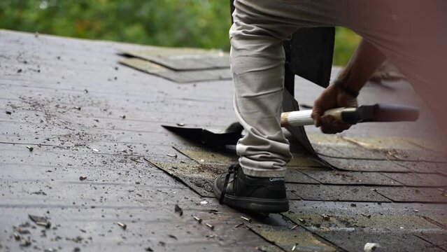 Closeup view of roofer removing old roof shingles as part of a house renovation project in slow motion