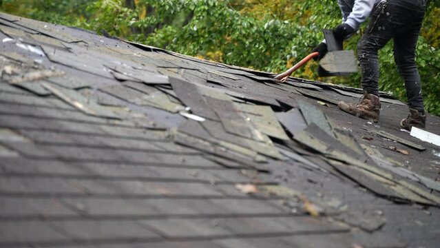 Closeup view of roofer removing old roof shingles as part of a house renovation project in slow motion