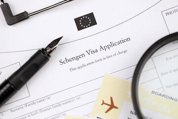 Schengen visa application on A4 tablet lies on office table with pen and magnifying glass close up