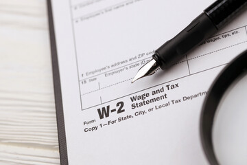 IRS Form W-2 Wage and Tax Statement blank on A4 tablet lies on office table with pen and magnifying glass close up