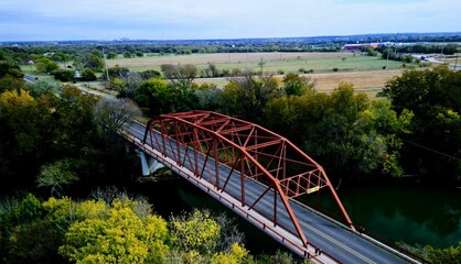 Drone shot of a red metallic structure on a bridge surrounded by lush trees