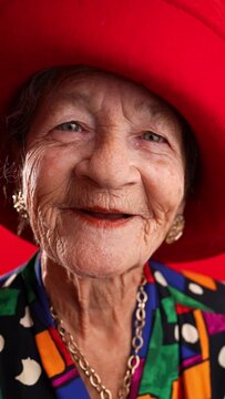 Vertical video of smiling fisheye portrait caricature of funny elderly woman smiling with red hat and no teeth isolated on red background.