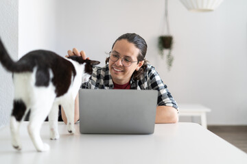 Cozy Productivity. Young Man in Plaid Shirt Petting Black and White Cat While Working