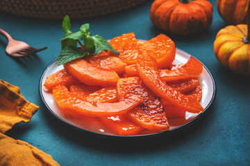 Baked pumpkin slices caramelized in orange glaze, autumn or winter dessert food on dark green table background. Top view