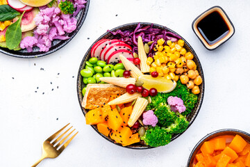 Vegan buddha bowl with sweet potato, quinoa, chickpeas, soybeans edamame, tofu, corn, cabbage, radish, broccoli and sesame seeds, white table background, top view. Autumn or winter healthy slow food