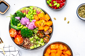 Vegan buddha bowl with baked pumpkin, quinoa, tomatoes, spinach, celery, radish, soybeans, edamame, tofu, cauliflower, broccoli and sesame seeds, white table background, top view. Autumn slow food