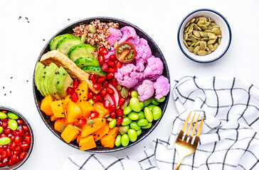 Vegan buddha bowl with pumpkin, quinoa, avocado, edamame soybeans, fried tofu, cauliflower, pomegranate and seeds, white table background, top view. Autumn or winter healthy vegetarian slow food