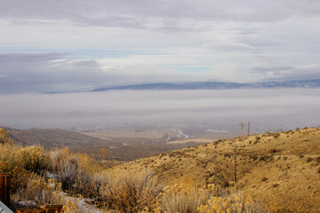 An oblique panorama with dry grass in the foreground, a landscape with roads, fields, meadows, mountains that are hidden in clouds and fog on the horizon. Picturesque landscape with beautiful sky