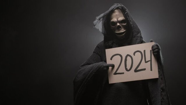 Grim reaper holding a 2024 sign in his hands and dancing, on a black background. Symbolism and superstition. New Year. Halloween characters concept.