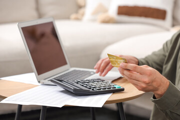Man with laptop, calculator and credit card planning budget at table indoors, closeup. Debt problem - obrazy, fototapety, plakaty