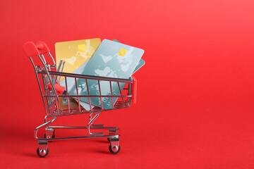 Small metal shopping cart with credit cards on red background, space for text