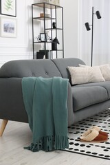 Comfortable sofa with green blanket, pillows and slippers in living room