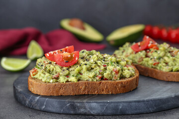 Slices of bread with tasty guacamole and ingredients on grey table, closeup