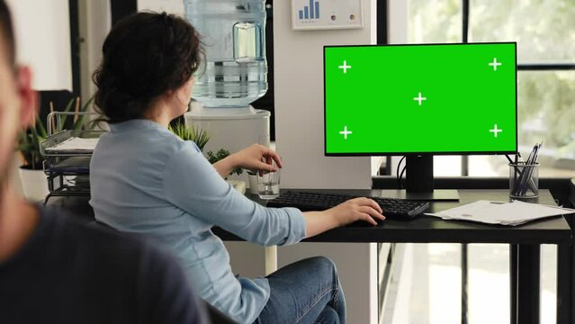 Office employee looks at greenscreen sitting at workstation, checking isolated chromakey display on computer monitor. Woman typing information and examining blank mockup desktop.
