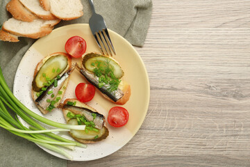 Delicious sandwiches with sprats, pickled cucumber and green onion served with tomatoes on wooden table, flat lay. Space for text