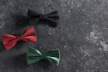 Stylish color bow ties on black textured background, flat lay. Space for text