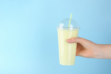 Woman with plastic cup of tasty smoothie on light blue background, closeup. Space for text