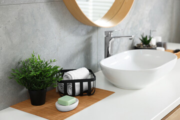 Potted artificial plant, rolled towels and soap near sink on bathroom vanity