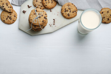 Tasty chocolate chip cookies and glass of milk on white wooden table, flat lay. Space for text