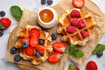 Delicious Belgian waffles with fresh berries and honey on white marble table, flat lay