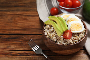 Tasty boiled oatmeal with egg, avocado and tomato served on wooden table, space for text