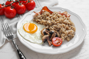 Tasty boiled oatmeal with fried egg, mushrooms, bacon and tomato served on white wooden table, closeup