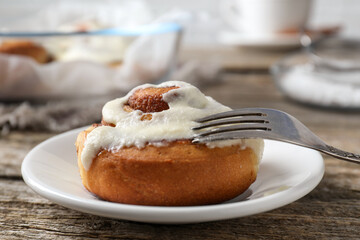Tasty cinnamon roll with cream on wooden table, closeup