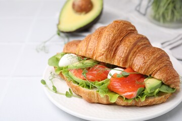 Tasty croissant with salmon, avocado, mozzarella and lettuce on white tiled table, closeup