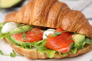Tasty croissant with salmon, avocado, mozzarella and lettuce on white table, closeup