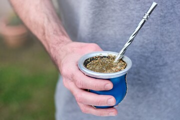 Hand of young caucasian man holding cup of mate, traditional infusion in many South American countries. Blurred background with copy space for text.
