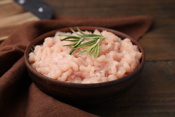 Fototapeta na wymiar Fresh raw minced meat and rosemary in bowl on wooden table, closeup