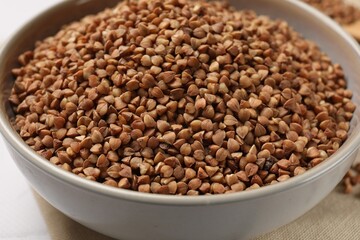Bowl with dry buckwheat on table, closeup