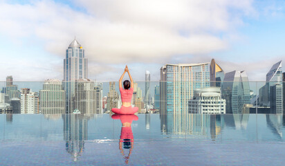 Asian woman pose yoga action on hotel rooftop with Bangkok city and swimming pool background