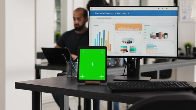 Empty desk with greenscreen tablet and computer running operational data, coworking space for business tasks. Computer desktop at workstation with blank chromakey mockup software on gadget.