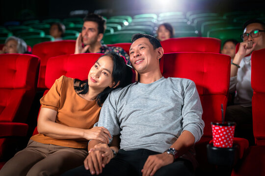 Happy trip of asian couple sweet sit togather on red seat and looking  movie in cinema
