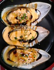 Fresh mussel with cheese sauce on black plate. Selective focus.