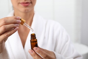 Woman with bottle of cosmetic serum and dropper on light background, closeup