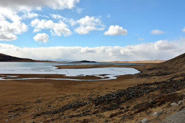 A beautiful huge lake captured by the first ice in the valley at the foot of a gently sloping mountain on a sunny day.