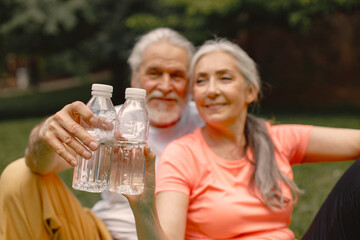 Focus on bottles of water in hands of senior couple at park