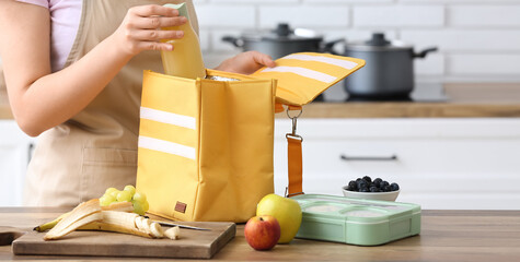 Woman putting bottle of juice into lunch bag in kitchen