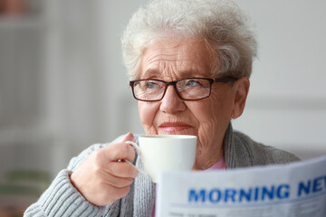 Senior woman with newspaper drinking coffee at home, closeup - obrazy, fototapety, plakaty