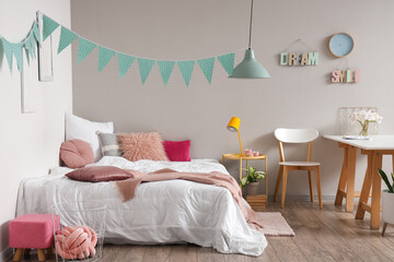 Interior of children's bedroom with cozy bed, table and garland