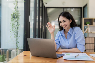 Ambitious Asian girl working from home Looking at laptop screen and financial documents, woman is checking email or doing research while working remotely.