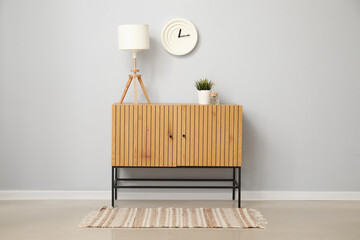 Wooden cabinet with table lamp and houseplant near white wall